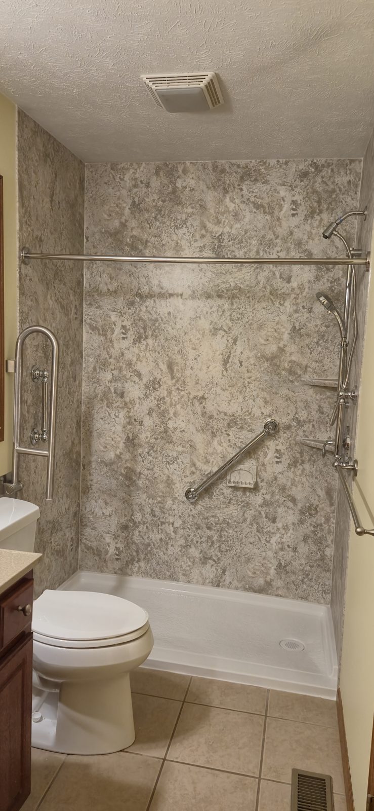 Bathroom with a shower grab bar and a fold-up grab bar next to the toilet