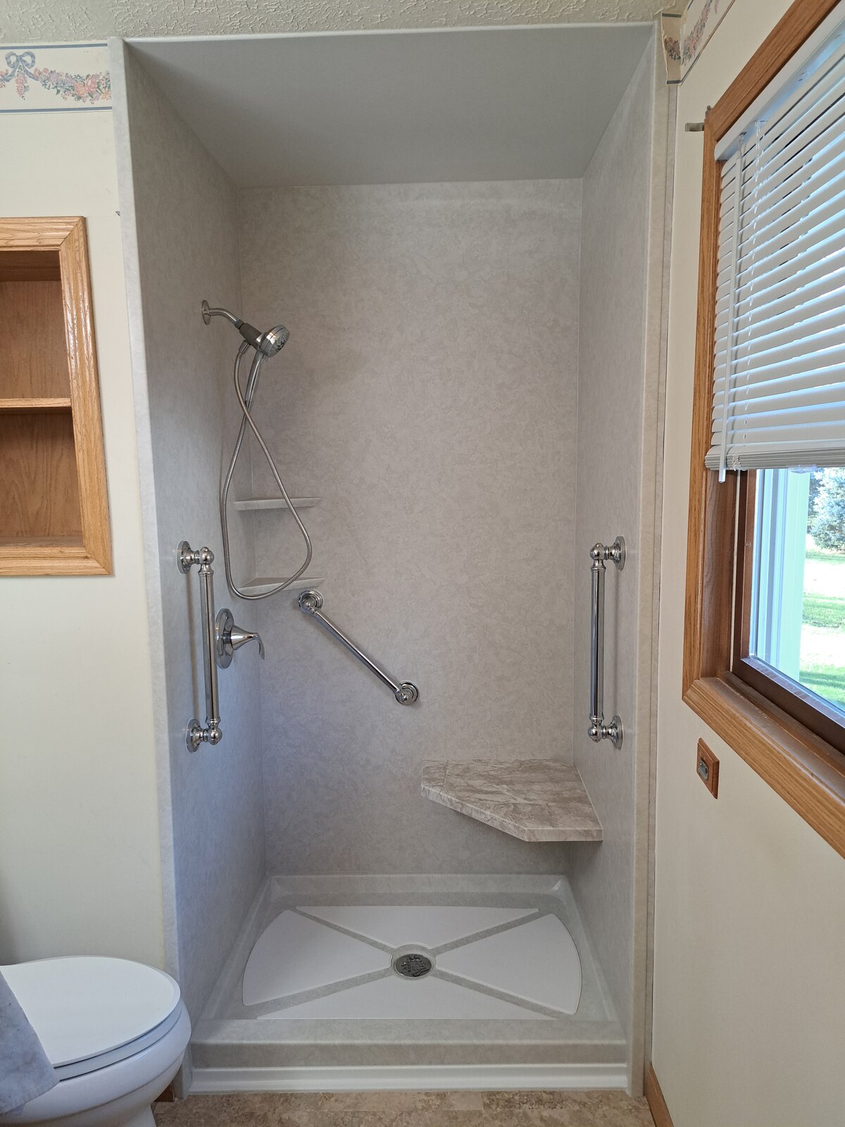Finished shower with handheld showerhead, grab bars and corner shelf