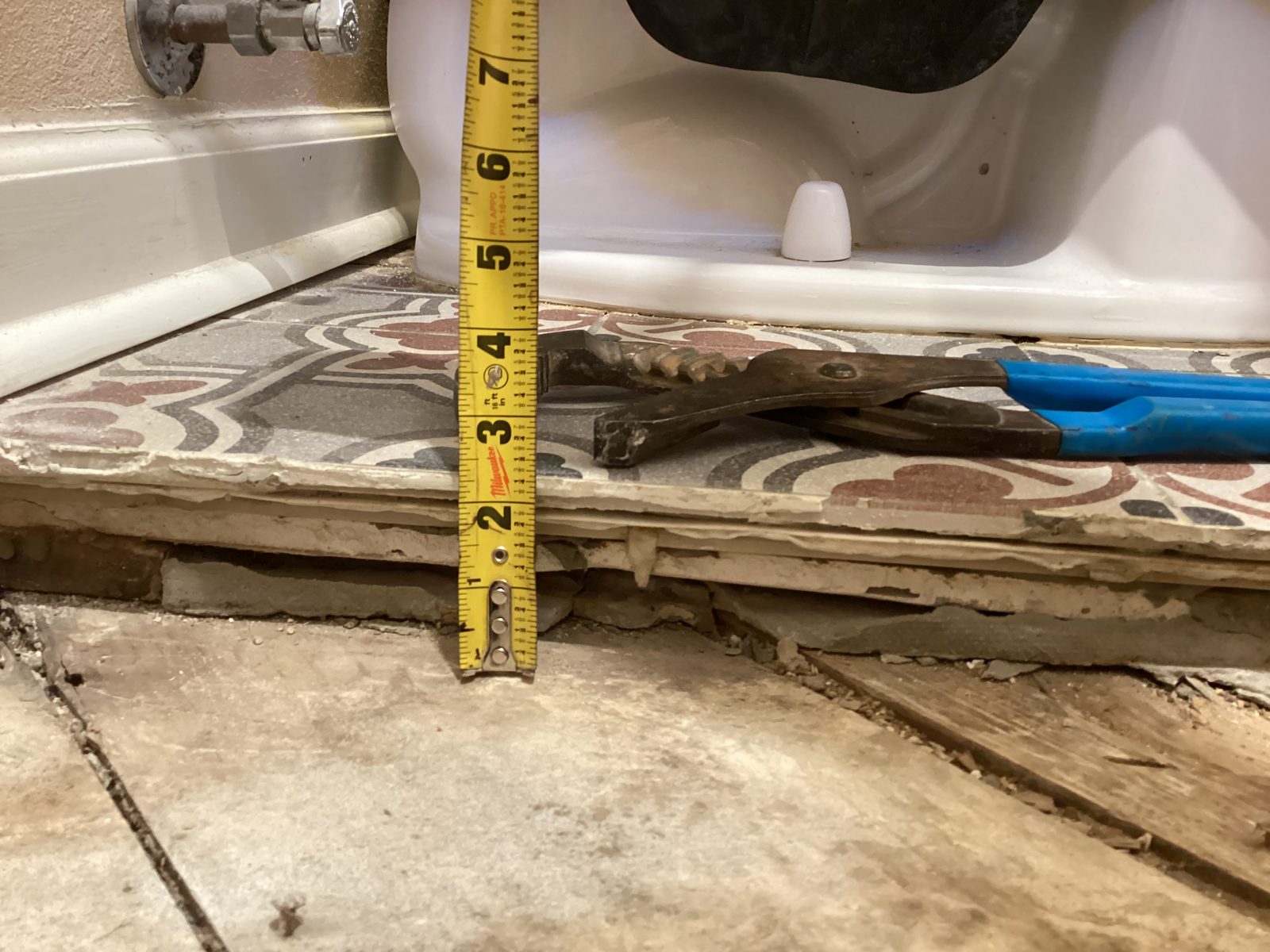 Tape measure showing the depth of the layered old flooring at the tub-to-shower conversion
