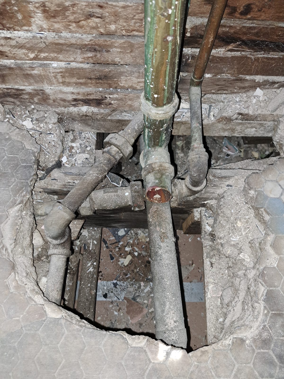 Floor opened at the old tub location, showing original drain piping beneath the hex tile