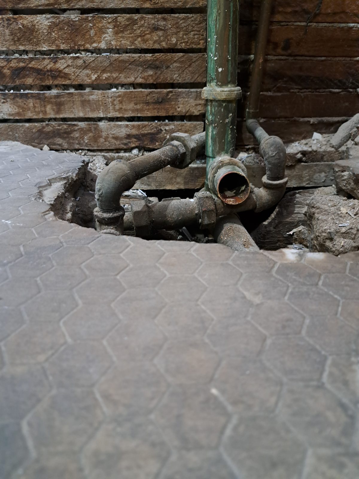 Original drain and supply piping exposed beneath the bathroom floor