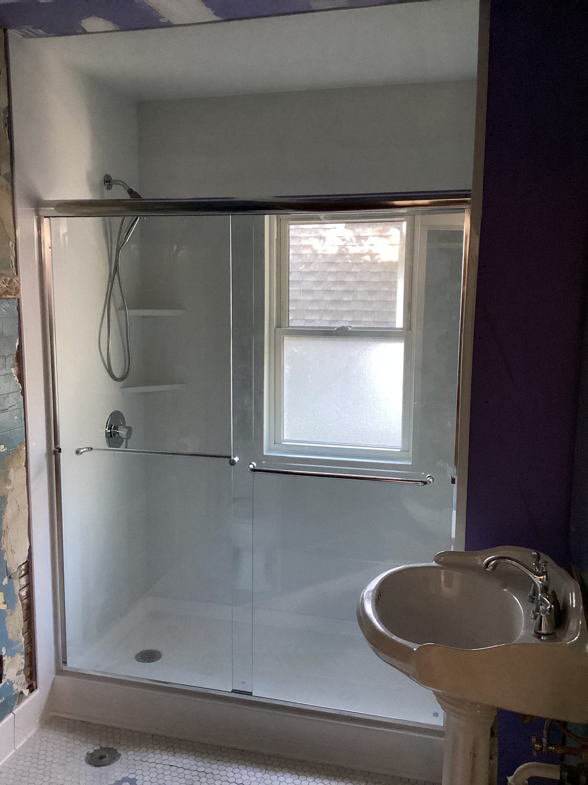Finished white shower with sliding glass door and a wall surround wrapped around the window