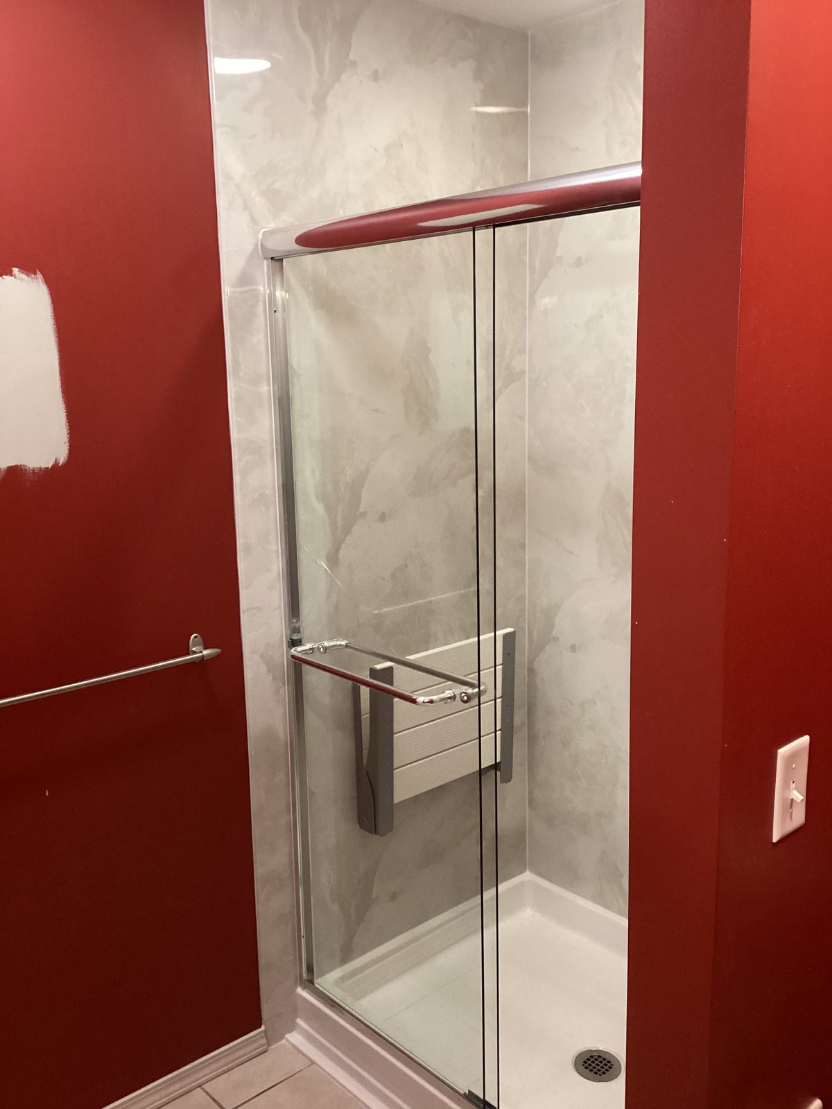 Fold-up shower seat and diagonal grab bar inside a marble-look shower