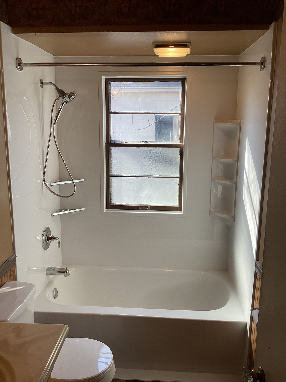 New white bathtub and smooth wall surround fitted around an existing wood window
