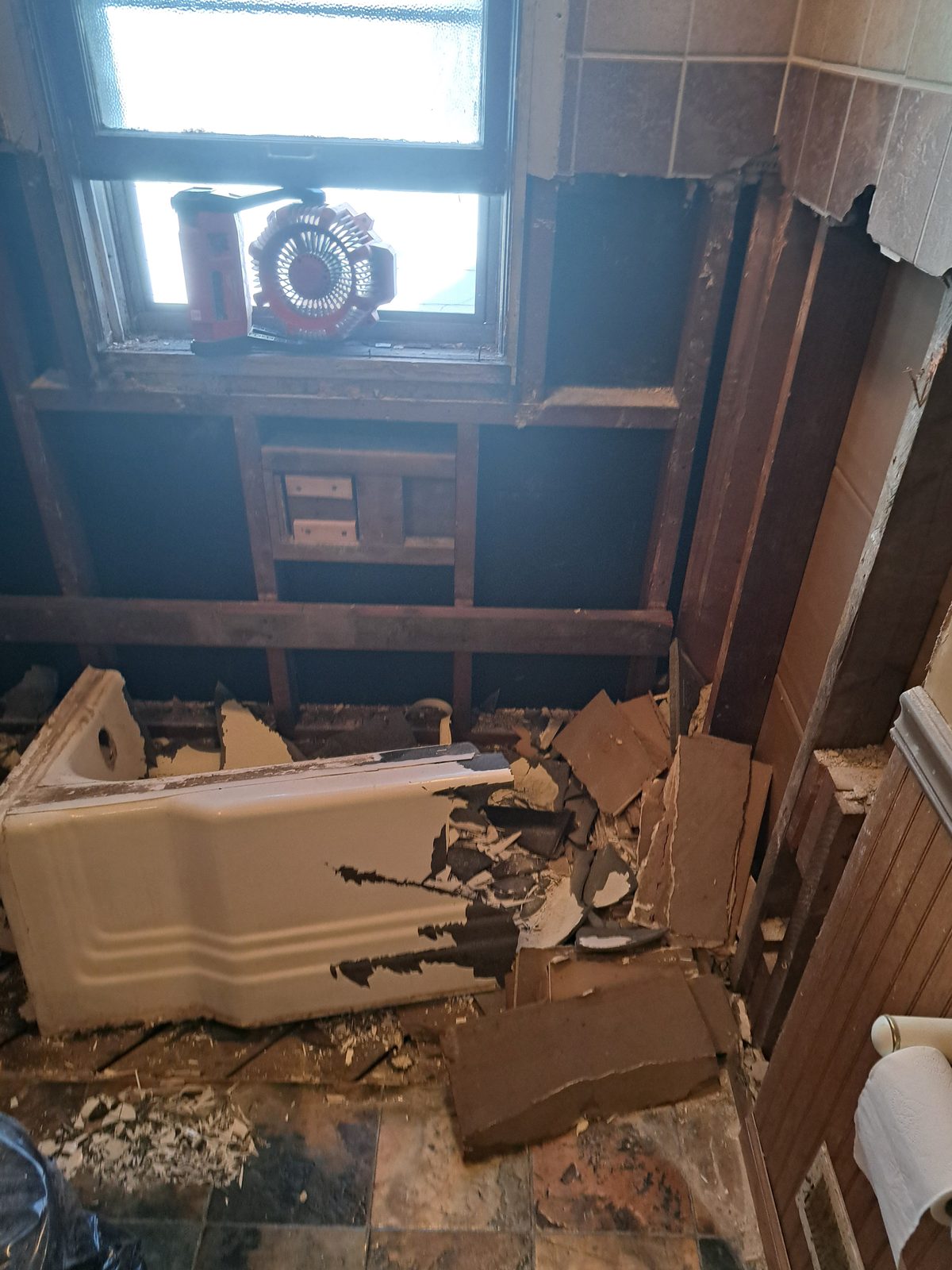 Old cast-iron bathtub broken into sections with the wall opened to the framing below the window