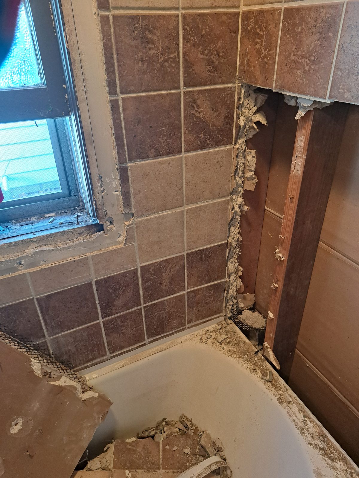 Old tile and thick mortar backing being removed beside a bathroom window