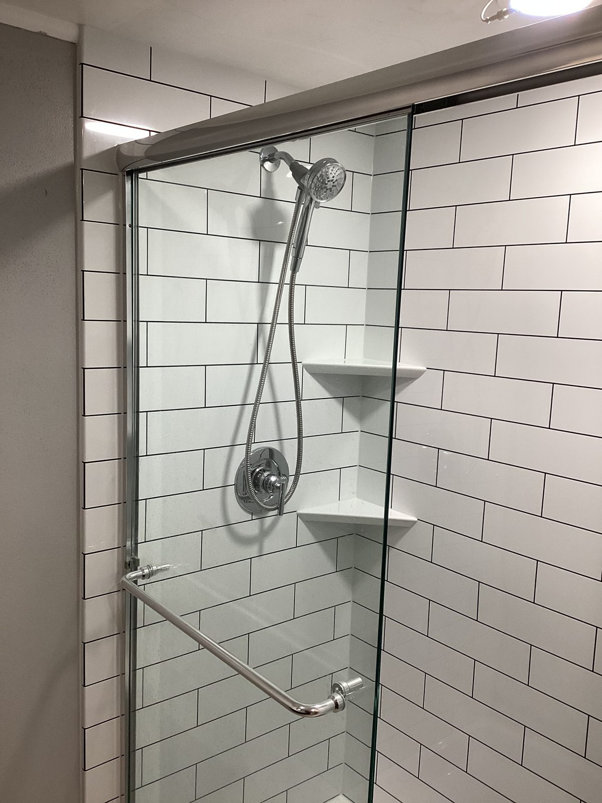 Chrome handheld shower head and valve against white subway tile
