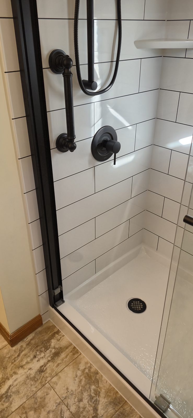 Matte black grab bar and shower valve in a modern subway tile shower